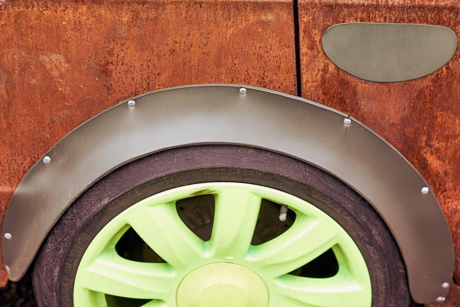 Close-up of a rusted car panel and wheel well showing corrosion behind the fender