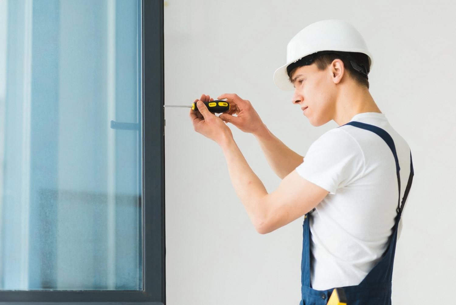 Technician in overalls repairing a window frame inside a Dubai apartment